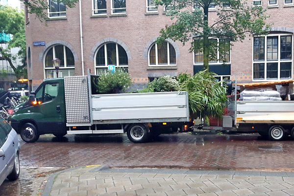 Bedrijfswagen met aanhanger vol palmen en beplanting voor een daktuin in Amsterdam
