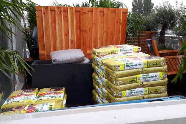 Zakken potgrond aangevoerd op een dakterras met houten schutting